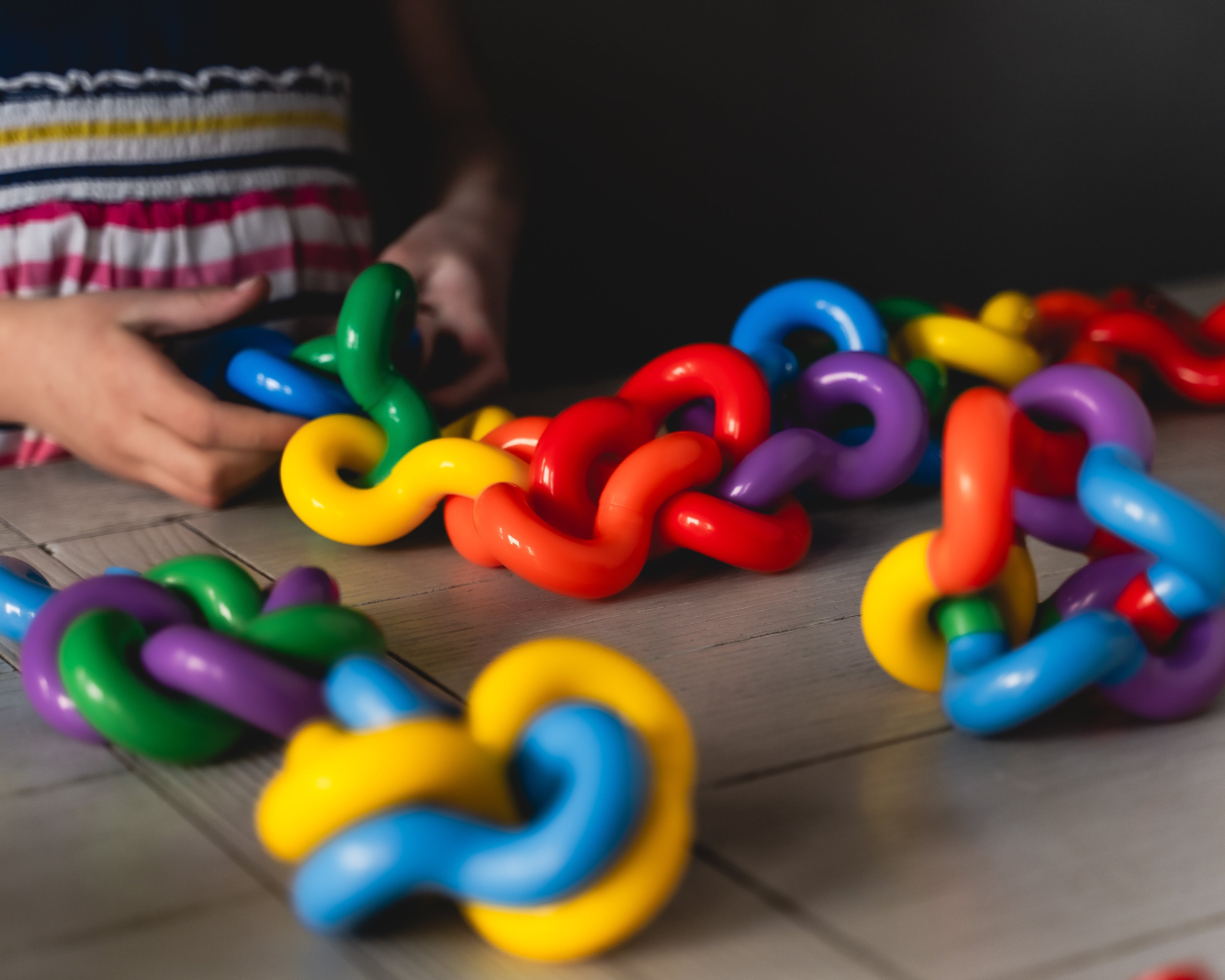 Colorful toy links on a tiled floor with a child's hands interacting with them.